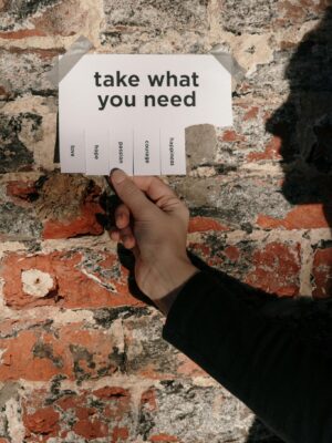 A hand holding a paper note with motivational text against a rustic brick wall.