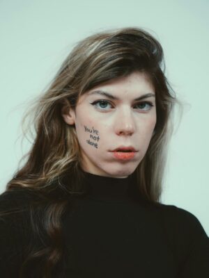 Close-up portrait of a person with 'You're Not Alone' written on their cheek.
